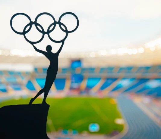 ‘I don’t believe in paying athletes’, says IOC President Statue of athletics Woman holding above head olympic circle. Modern Olympic Stadium in Background. Sport photo for Summer olympic Game in Paris 2024.