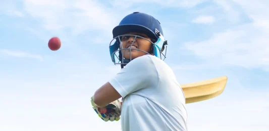 Female Indian cricket player wearing protective gear and hitting the ball with a bat on the field
