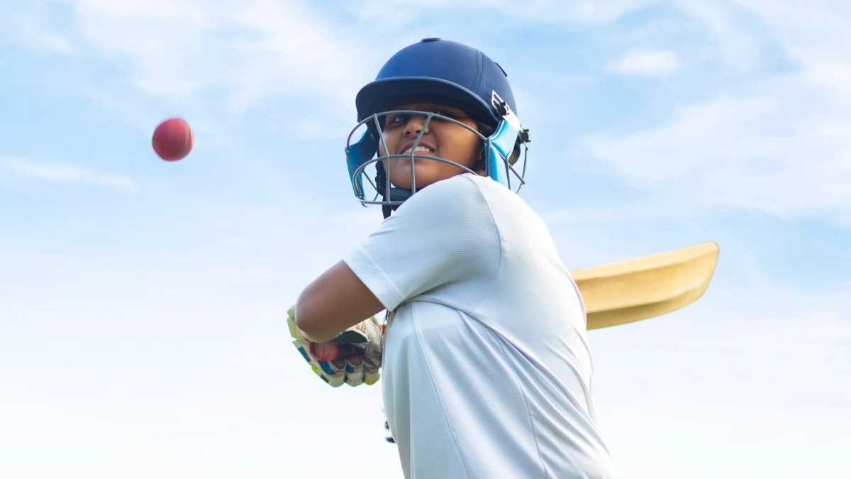 Female Indian cricket player wearing protective gear and hitting the ball with a bat on the field