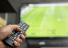 Premier League CEO and Andy Burnham face 3pm blackout heat close up Television remote control in casual man hand hold pointing to tv set and turning it on or off. select channel watching soccer game on tv his at home in the living room relax.