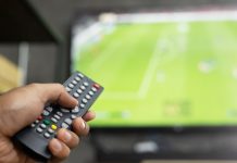 Premier League CEO and Andy Burnham face 3pm blackout heat close up Television remote control in casual man hand hold pointing to tv set and turning it on or off. select channel watching soccer game on tv his at home in the living room relax.