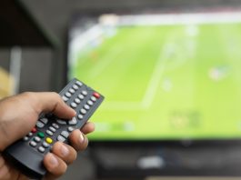 Premier League CEO and Andy Burnham face 3pm blackout heat close up Television remote control in casual man hand hold pointing to tv set and turning it on or off. select channel watching soccer game on tv his at home in the living room relax.
