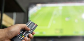 Premier League CEO and Andy Burnham face 3pm blackout heat close up Television remote control in casual man hand hold pointing to tv set and turning it on or off. select channel watching soccer game on tv his at home in the living room relax.