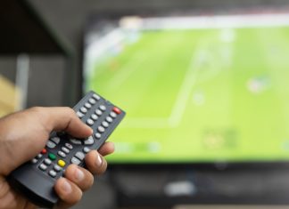 Premier League CEO and Andy Burnham face 3pm blackout heat close up Television remote control in casual man hand hold pointing to tv set and turning it on or off. select channel watching soccer game on tv his at home in the living room relax.