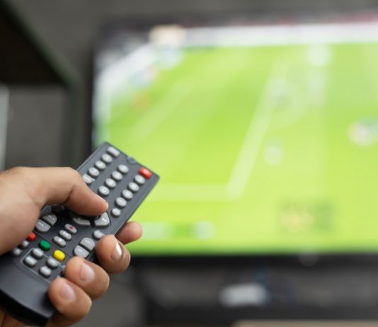 Premier League CEO and Andy Burnham face 3pm blackout heat close up Television remote control in casual man hand hold pointing to tv set and turning it on or off. select channel watching soccer game on tv his at home in the living room relax.