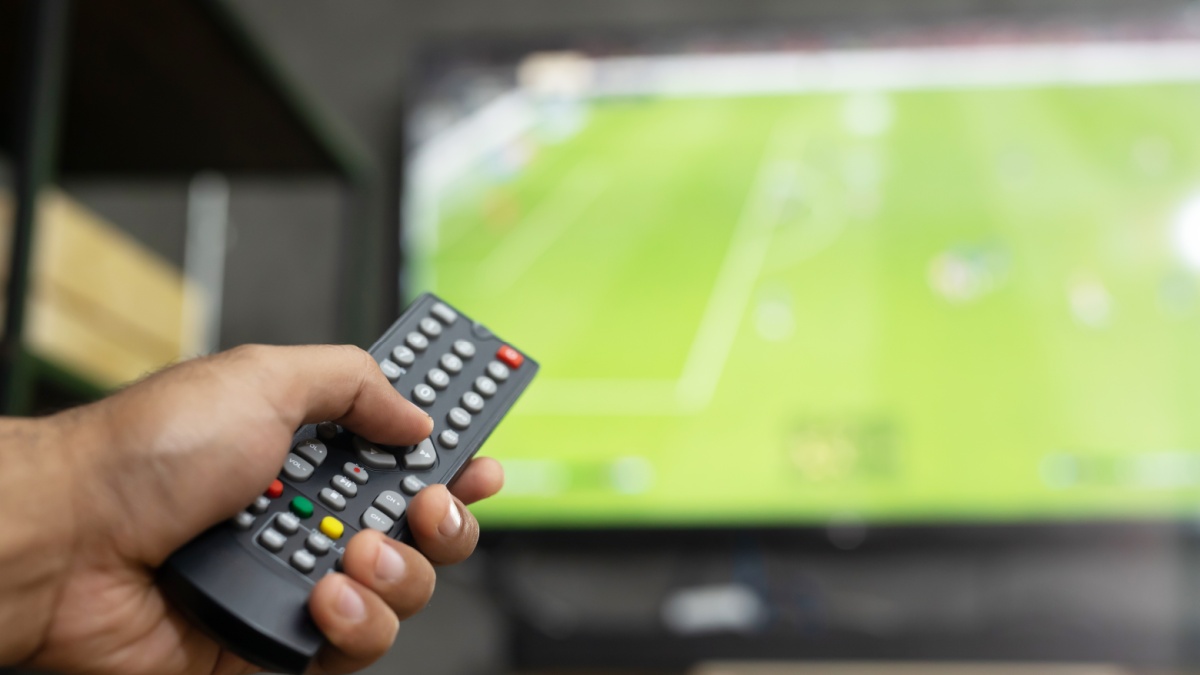 close up Television remote control in casual man hand hold pointing to tv set and turning it on or off. select channel watching soccer game on tv his at home in the living room relax.