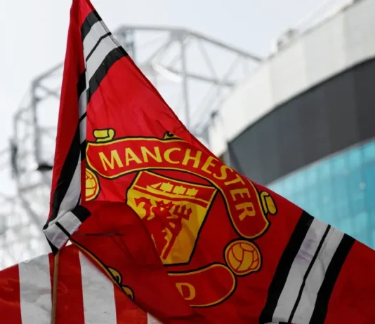 Disney+ finds backdoor into Manchester United’s fanbase Red Manchester United flag with club crest blows in the wind near Old Trafford stadium.